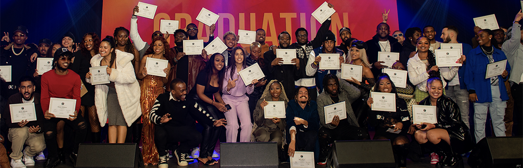 A group of graduates stand on a stage holding their certificates up.
