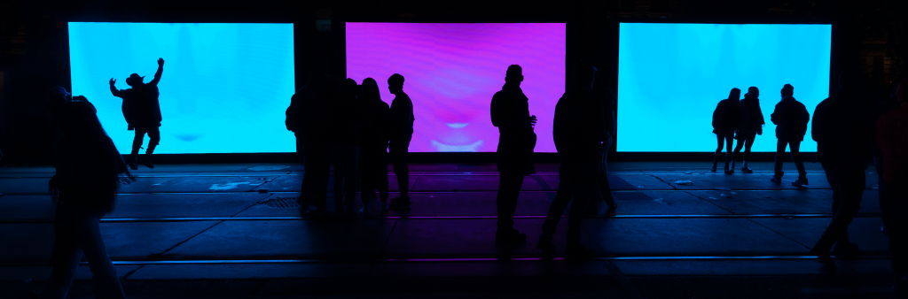 Shadows of people standing in front of large coloured screens