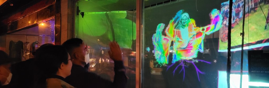 People look and wave at art projection in shop window