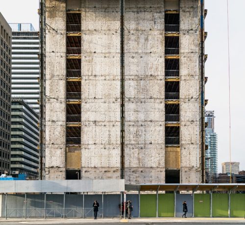 Colour photograph of unfinished concrete multi-story apartment building. with sidewalk in foreground.