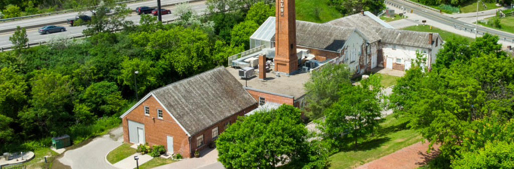 Aerial view of the Todmorden Mills building complex, surrounded by trees and greenery with the Don Valley parkway in the background.