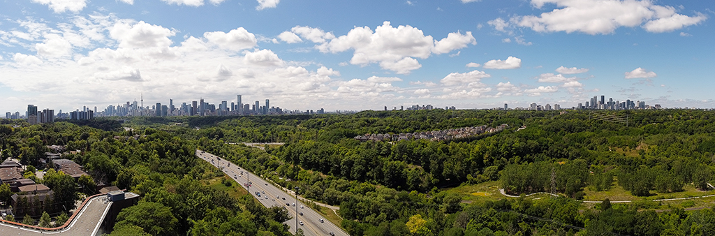 A heavily forested area that has houses and roads throughout. The Toronto skyline is in the background.