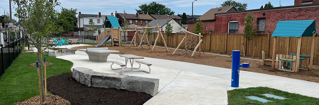 Path leading from the corner of Rogers Rd. and Nairn Ave to paved area with a picnic bench and an outdoor ping pong table. A bottle filler and drinking water fountain is located on the right side of the pathway.