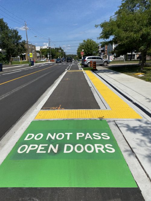 New raised bike lane with green and white pavement markings that read "Do not pass open doors".