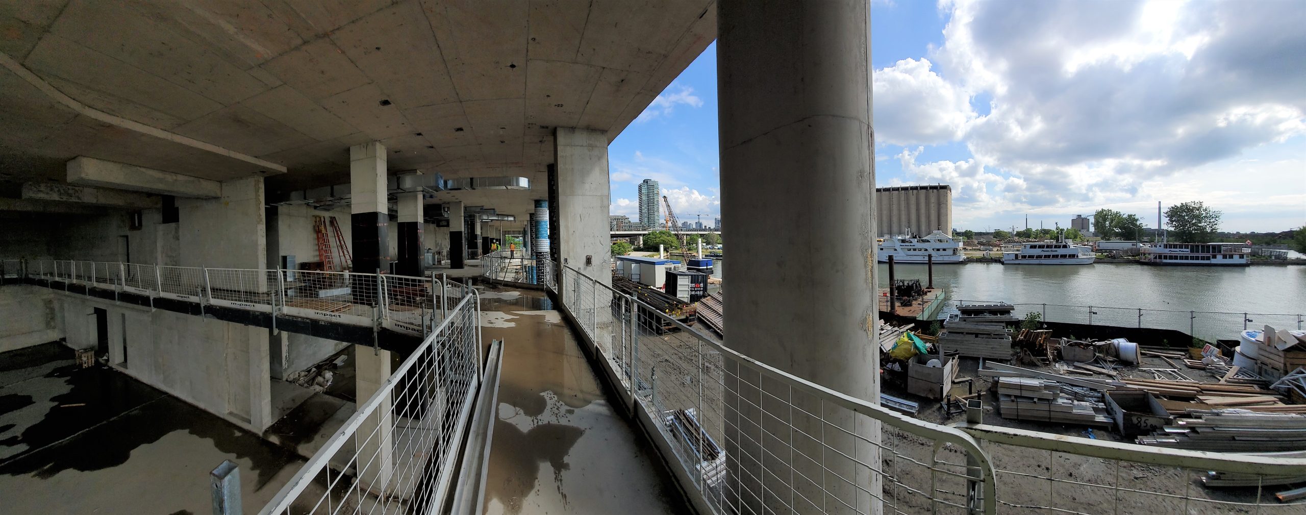 Interior of the new community recreation centre looking north from the walking track in the gym, showing the 2nd floor multi-purpose room and community kitchen at the left side, and the water’s edge promenade below at the right side.