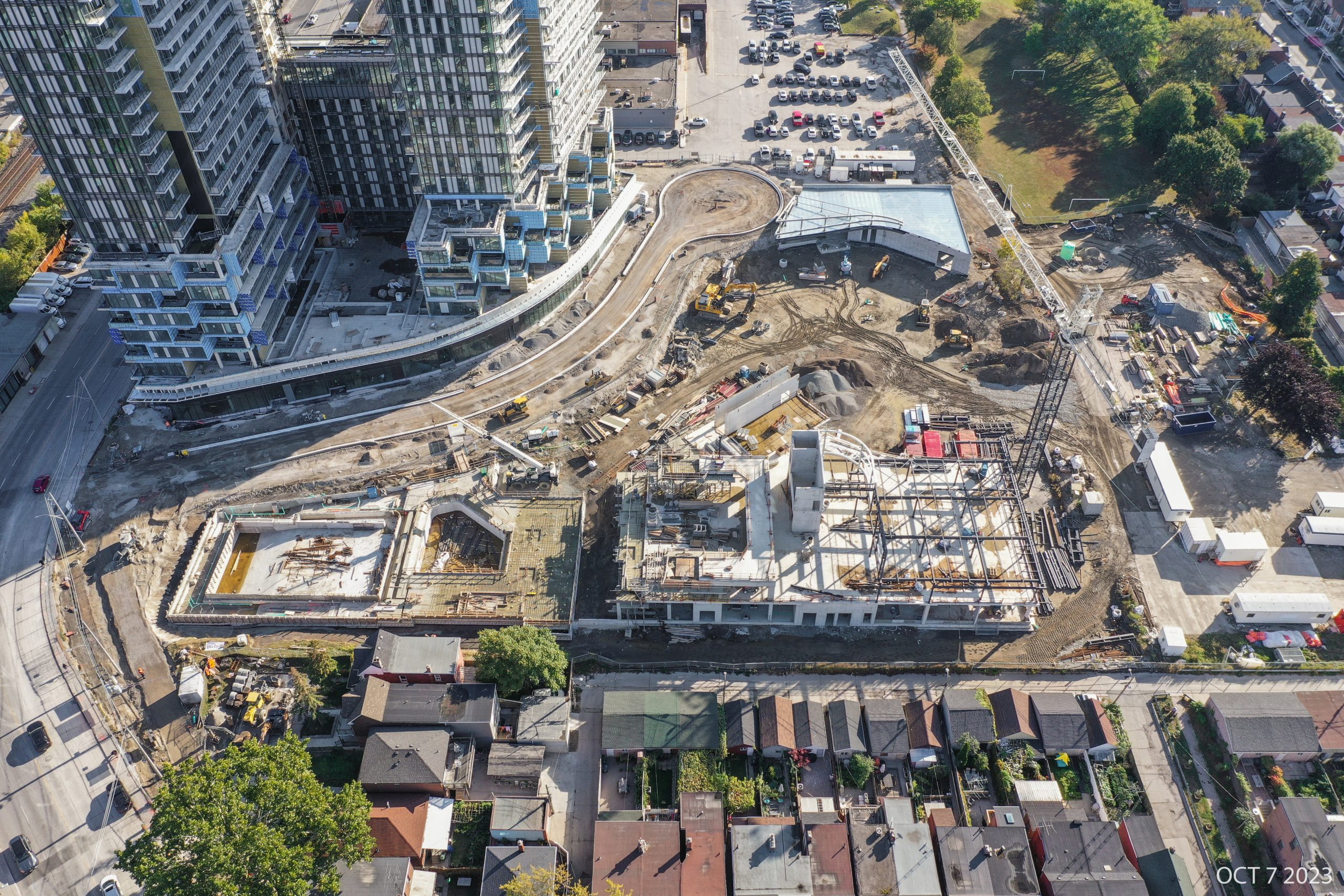 An aerial photograph of the construction site at Wallace Emersion Community Centre on October 7, 2023, which focuses on the community centre while under construction and the adjacent Fieldhouse. The community recreation structure is two-storeys with vertical beams being installed to the future third floor. The Fieldhouse is at ground-level with concrete walls and steel structural beams. 