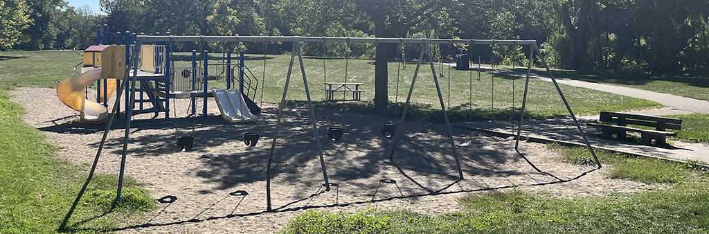 Cruickshank Park playground, with swings in the foreground and climbing equipment/slide in the background.