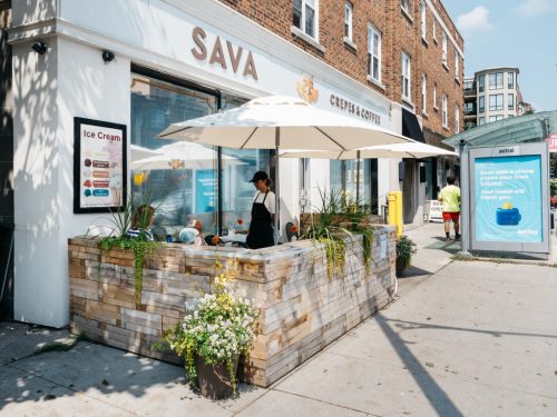Sava storefront with patio, umbrellas and flower pot on sidewalk