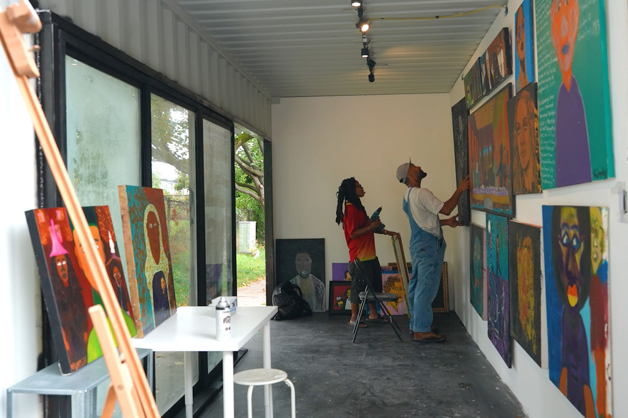 Two people hanging paintings in a shipping container