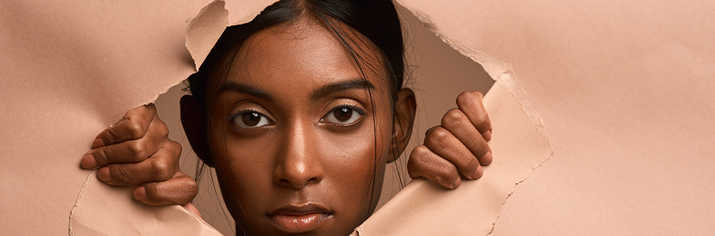 A black woman ripping open paper and looking through the hole in it.