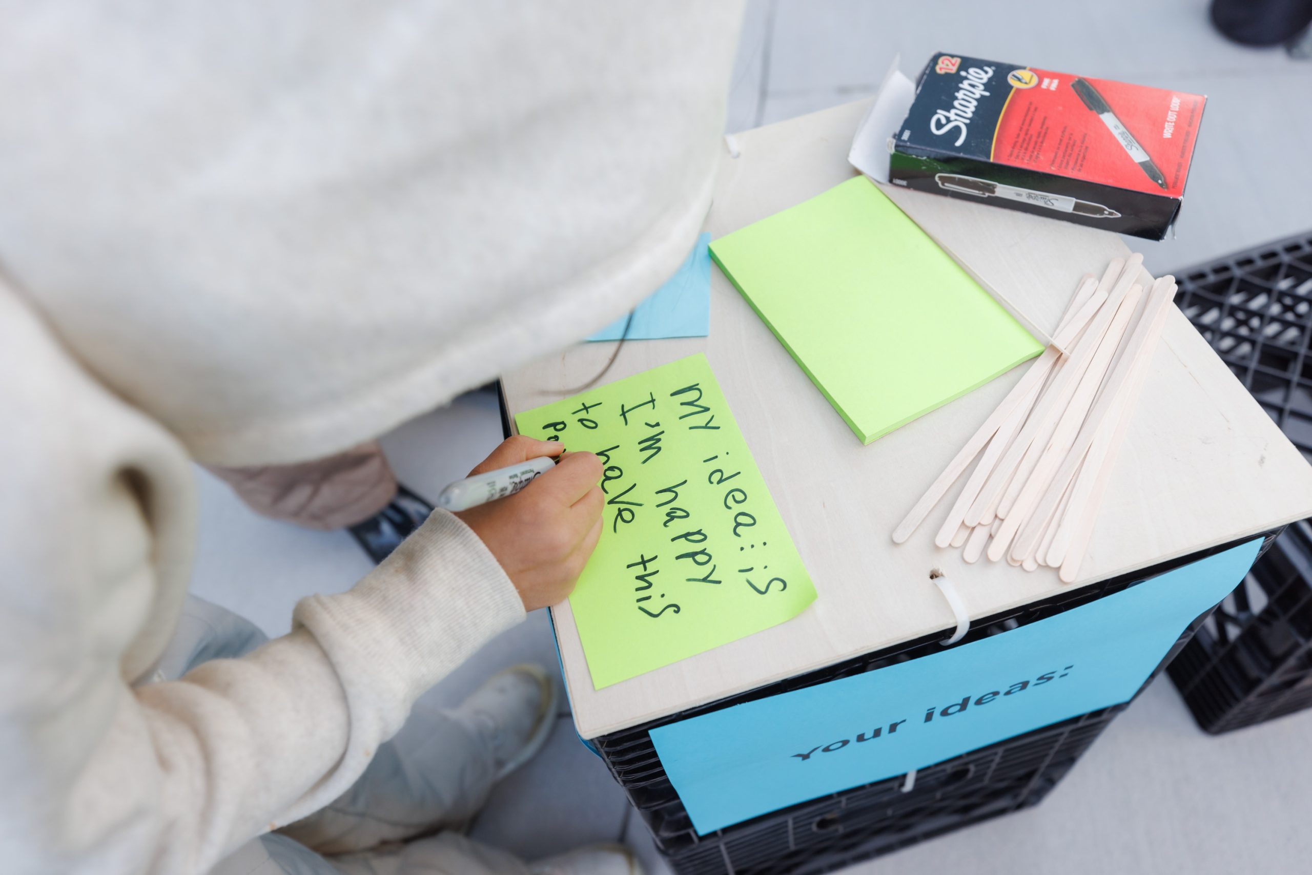 A member of the community writing their feedback on a sticky note to share an additional idea they have for the type of park character they want to see in the expanded Holmes Park.