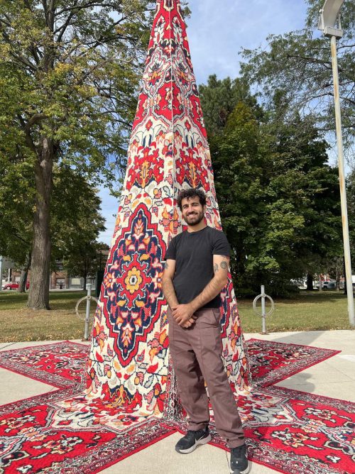 Picture of artist Roda Medhat, standing in front of art work in a park
