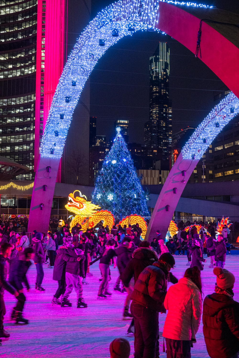 Lots of people skating with festive lights, a glowing Chinese Dragon and Christmas tree in the background