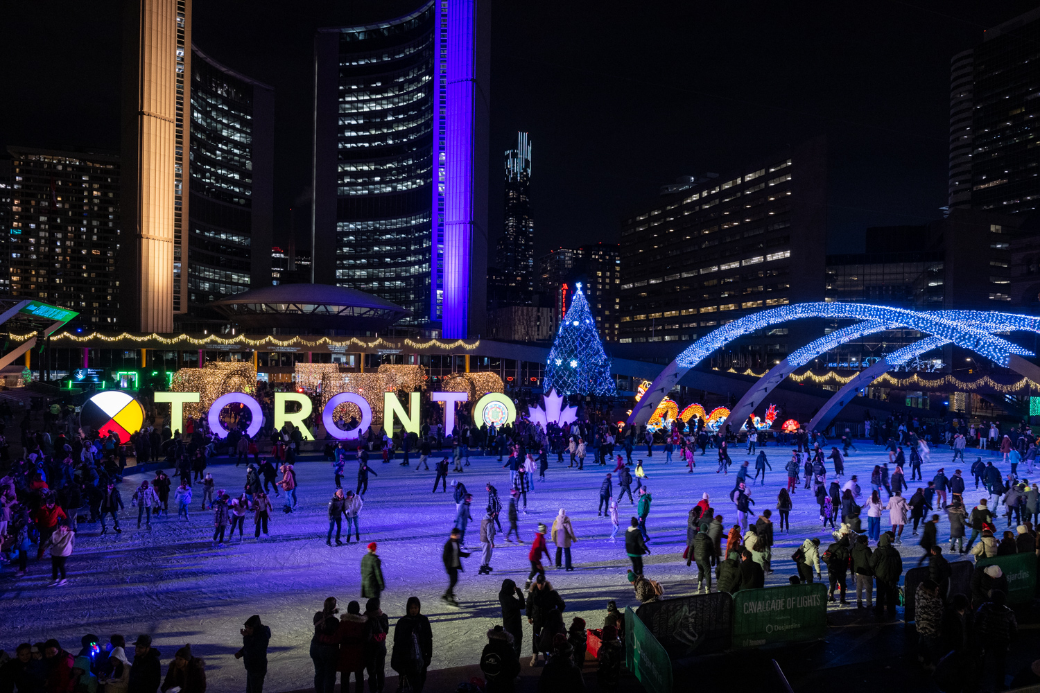 Wide shot of Nathan Phillips Square outdoor skating rink and Toronto Sign lit up with holiday festive lights