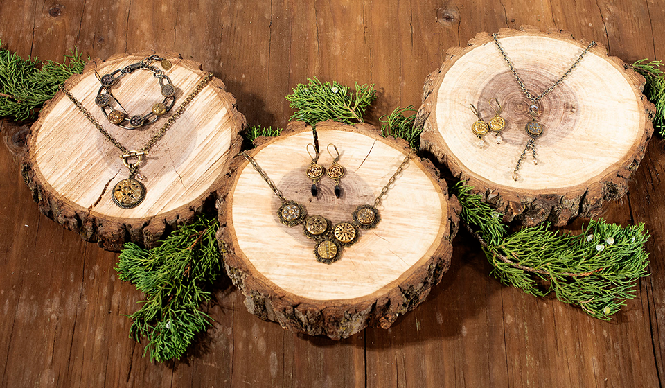 Necklaces, earrings and bracelet laid out on natural wood slices surrounded by evergreen branches