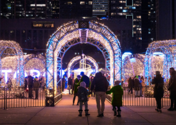 Visitors walking into Nathan Phillips Square, decorated with lighted archways and Toronto sign lit up in background.