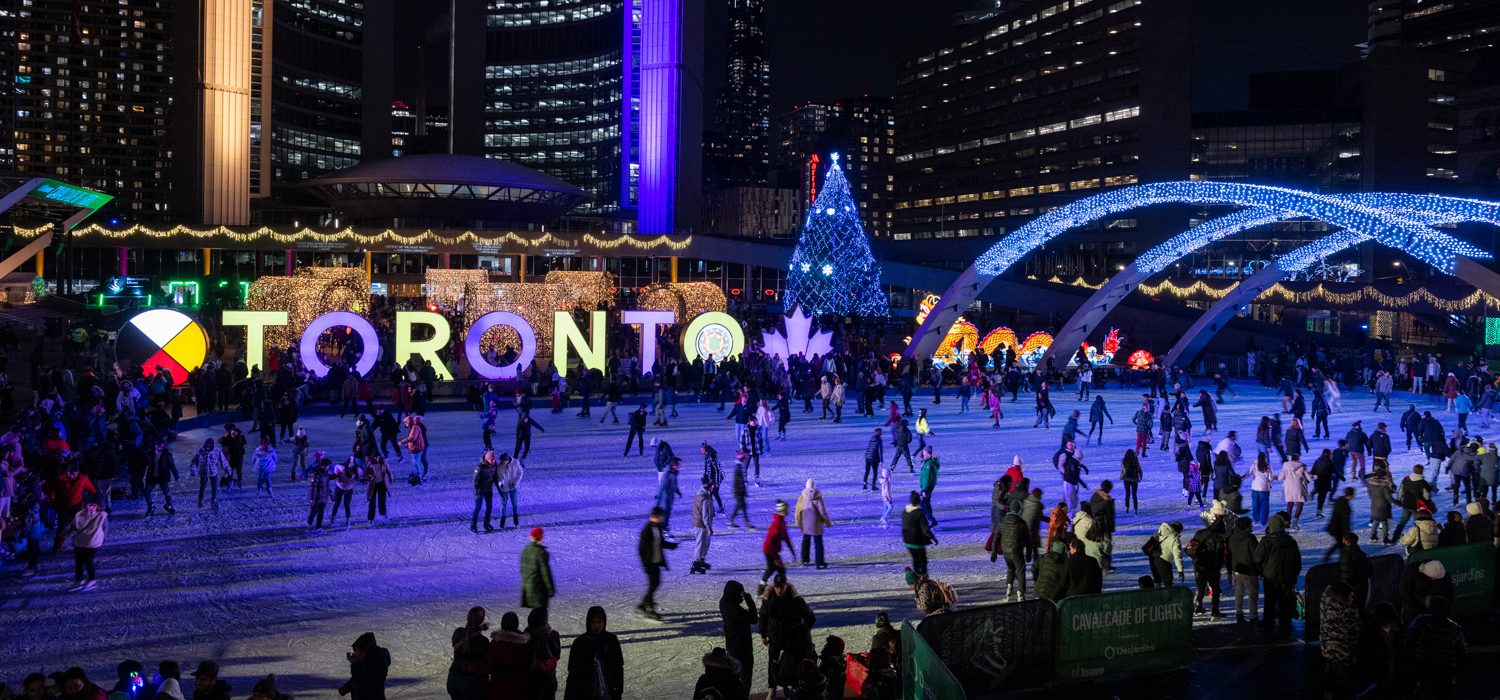 Wide shot of Nathan Phillips Square outdoor skating rink and Toronto Sign lit up with holiday festive lights