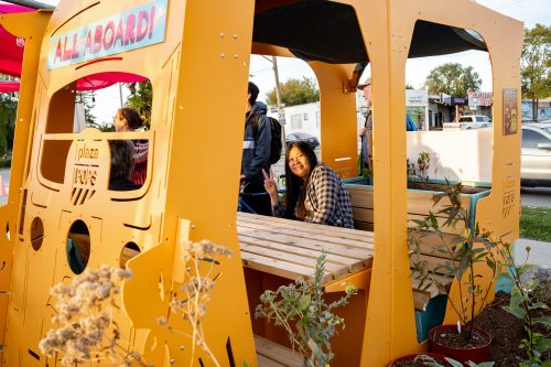 Person seated inside a tuk-tuk giving a peace sign. Signs on tuk-tuk reads All Aboard and plazaPOPS