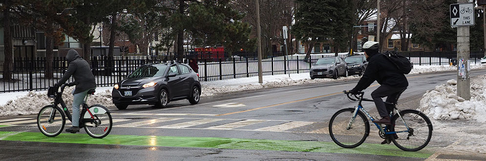 Two people cycle in winter through an intersection