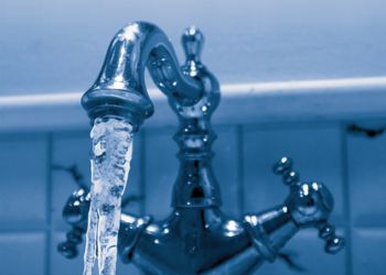 Chrome bathroom sink tap with frozen water coming out.