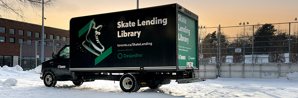 The Skate Lending Library van parked in front of an outdoor skating rink in winter.