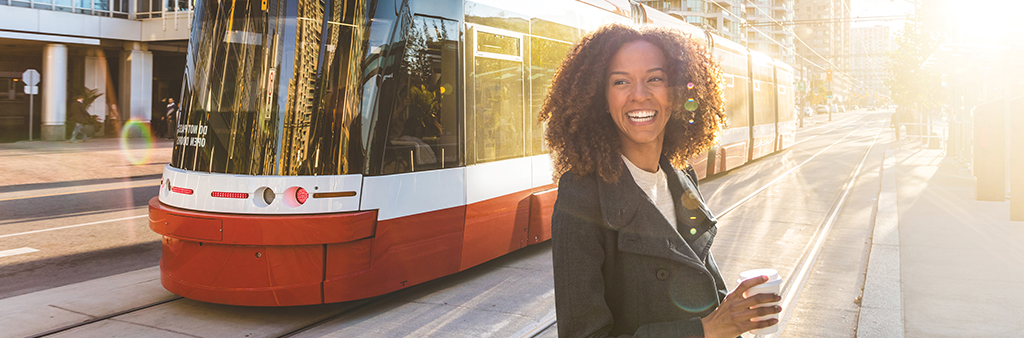 Smiling young woman crossing a street, holding a paper cup with a TTC streetcar in the background.