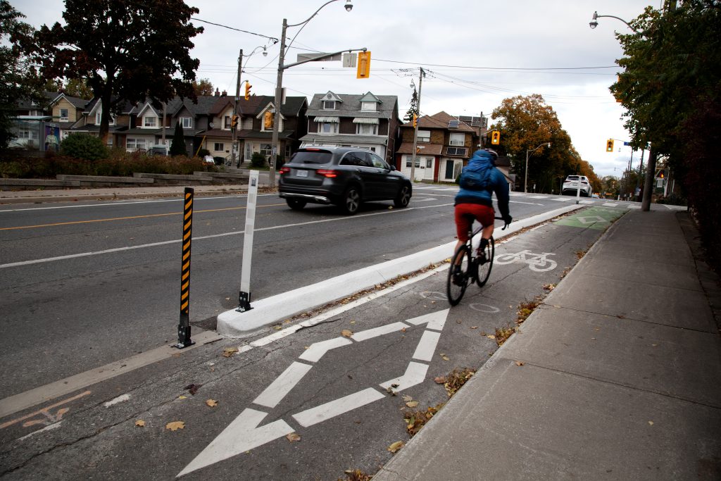 A person cycles in a bike lane protected from motor vehicle traffic by poured concrete curbs. 