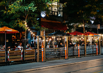 People sitting a curb lane patio enjoying a meal in the evening.