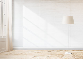 Empty room with a white wall in the background, window drapes on the left and a floor lamp on the right.