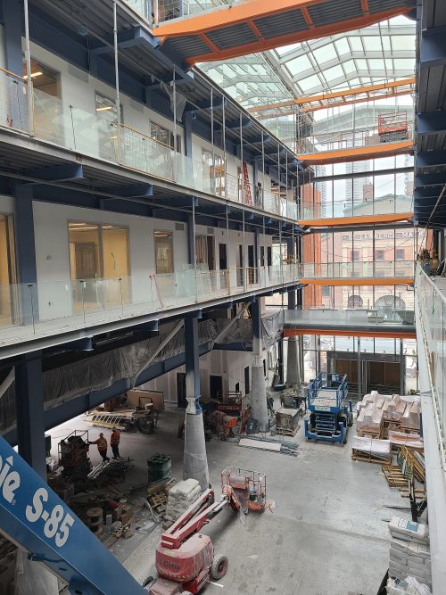 Interior view of the St. Lawrence Market, North Market Building showing piles of stone, machinery and construction workers.