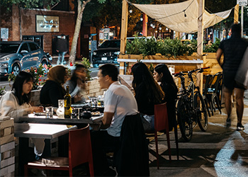 Wide shot of a curb lane patio at night time filled with people enjoying a meal.