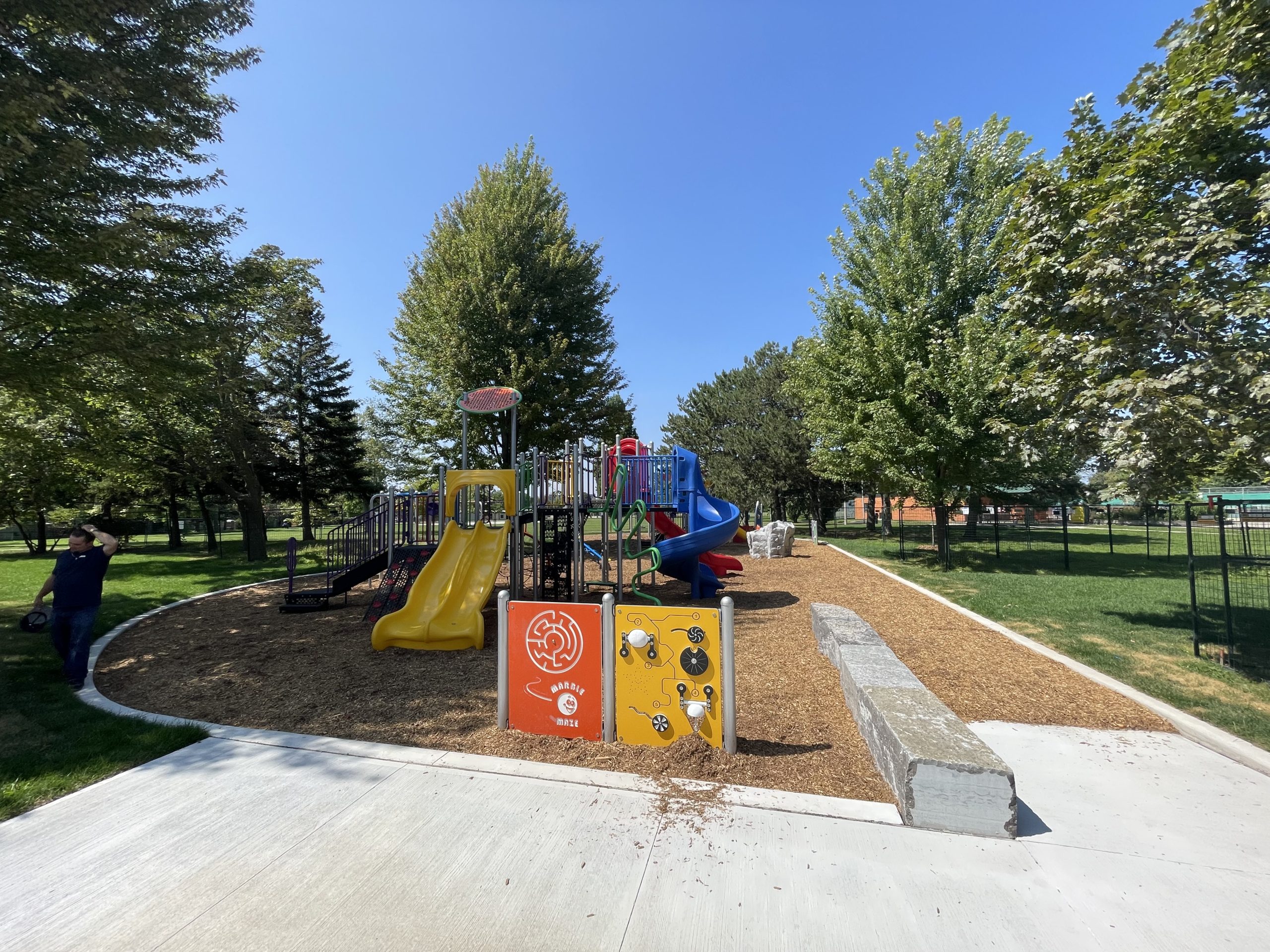 The new playground. The three slides are visible, along with some play panels. The mulch surfacing is surrounded by pavement.