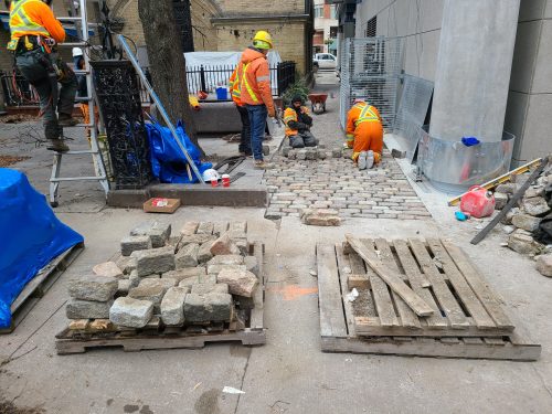 Construction workers landscaping exterior of St. Lawrence Market, North Building with stones and pieces of wood behind them.