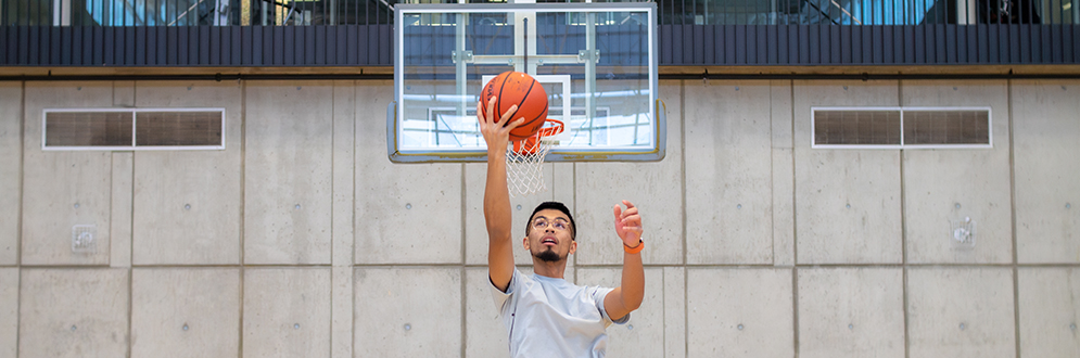 A person is dunking a basketball into a hoop at an indoor gym at York Recreation Centre.
