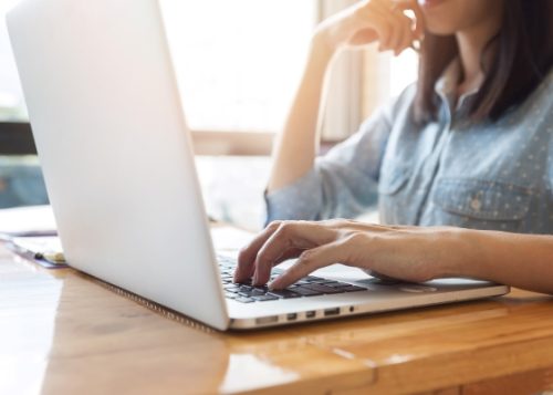 a sideview person sitting at a laptop with their hand on the keys