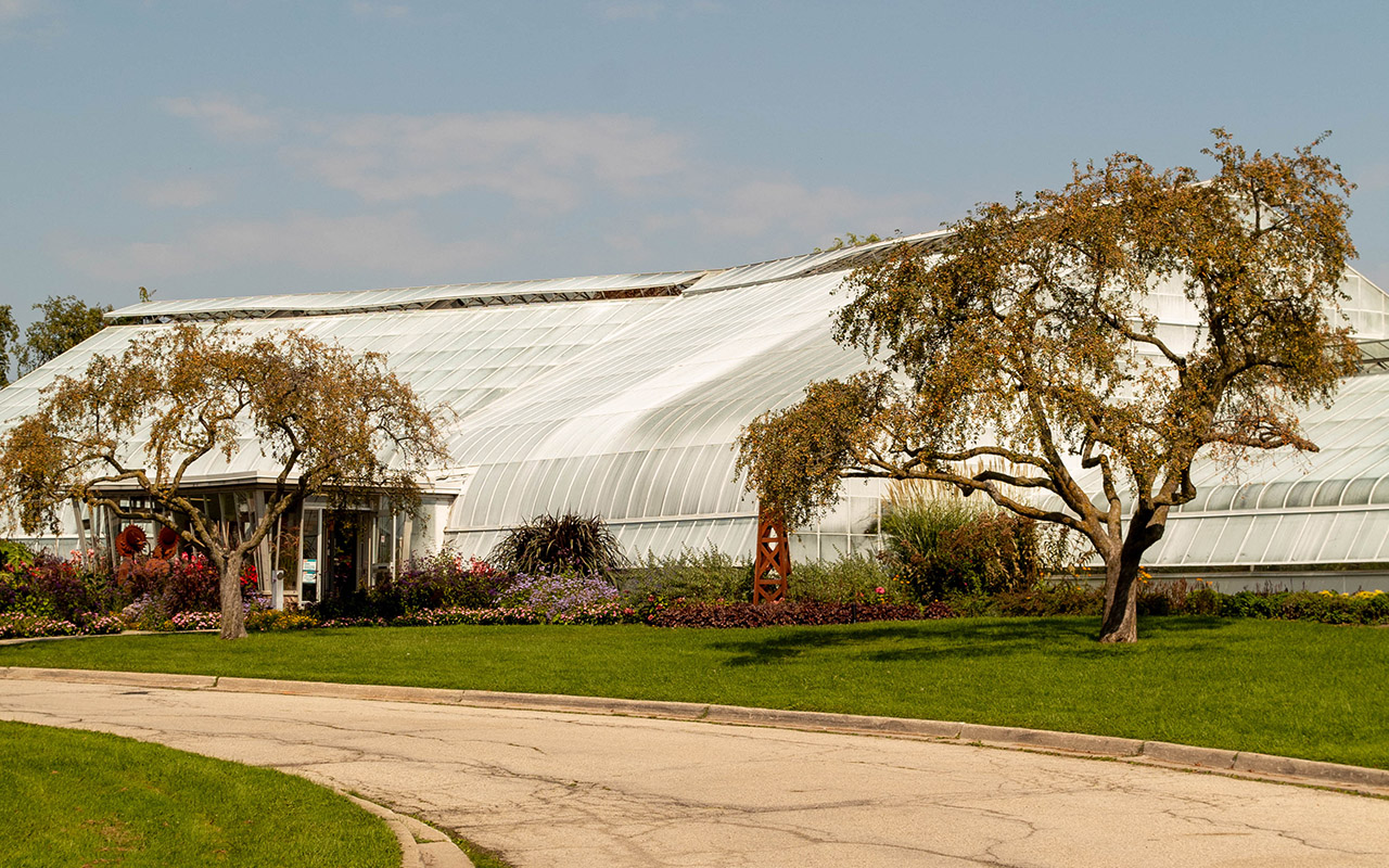 A large building made up of a few white greenhouses of differing heights. A road curves in front.