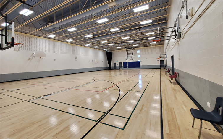 A photo of the gymnasium in Goulding Community Centre showing shiny beige refinished floors with new games lines in black and red.