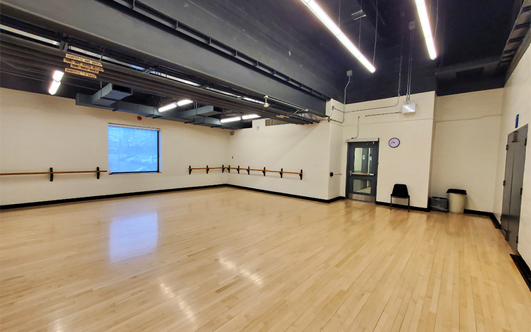 A photo of the dance studio in Goulding Community Centre which shows shiny beige floors, a window and an exit in the distance.