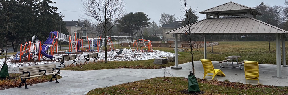Playground equipment, next to a covered picnic area. A paved path connects the two.