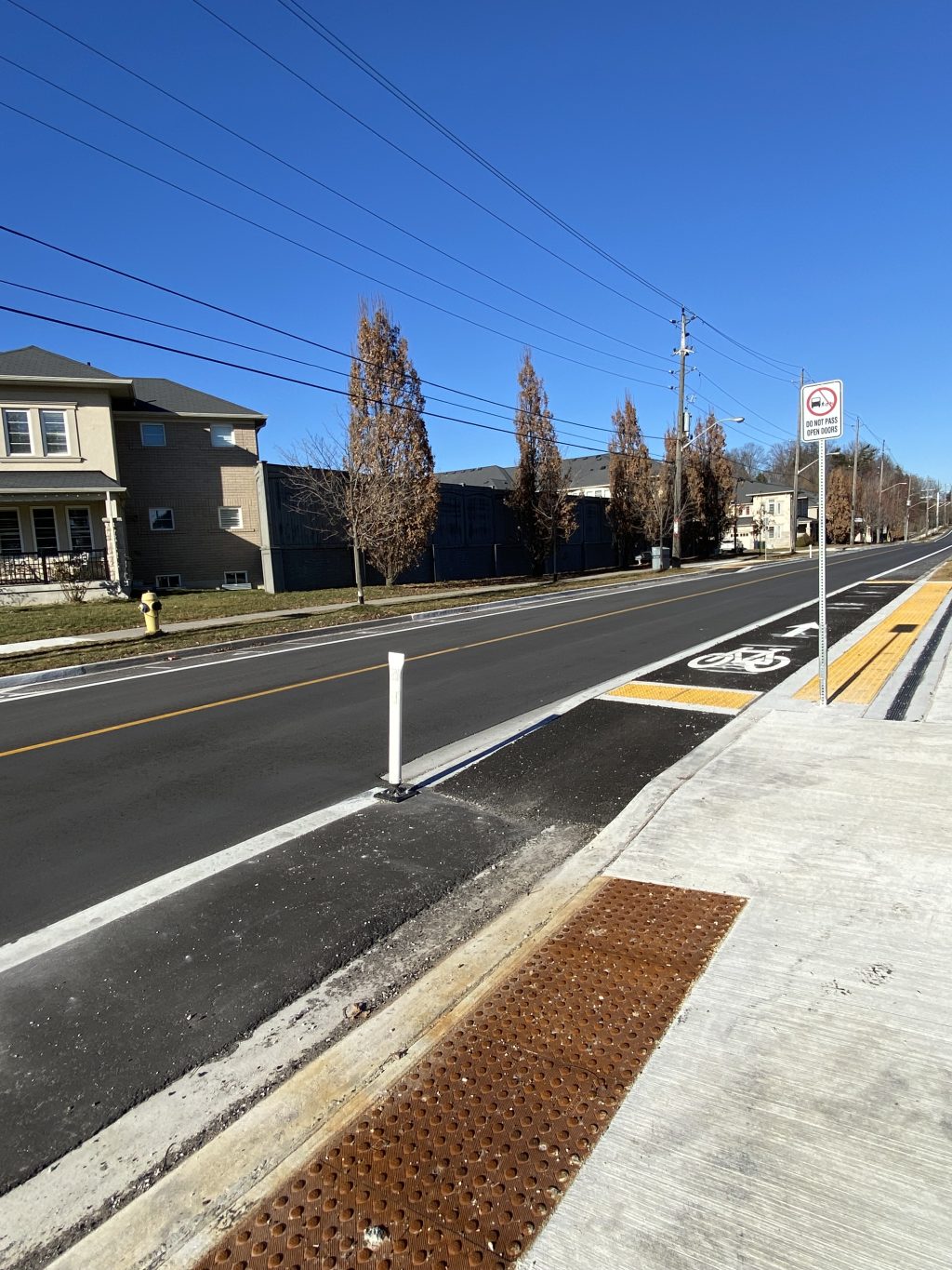 An integrated bus/bike platform is shown in a bike lane on Lawrence Ave E, with a sign reminding people cycling to not pass open doors to the right of the platform. 