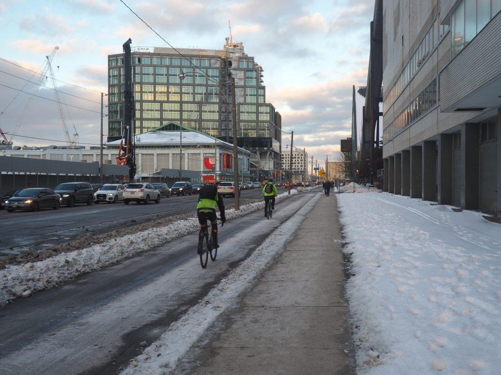 People cycle on the Martin Goodman Trail in the winter. Snow is placed between the trail and roadway.