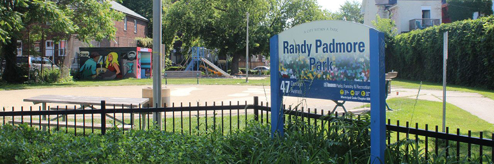 The Randy Padmore Park sign, nestled in a horticultural bed. The playground is in the background.