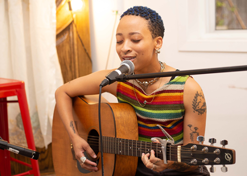 Seated musician singing into a microphone and playing the guitar.