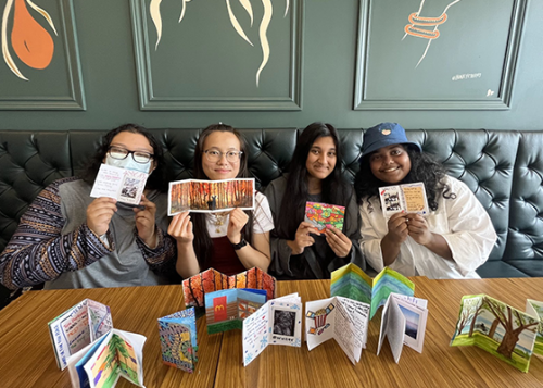 Four people sitting behind a table holding up cards, more cards are displayed on the table as well.