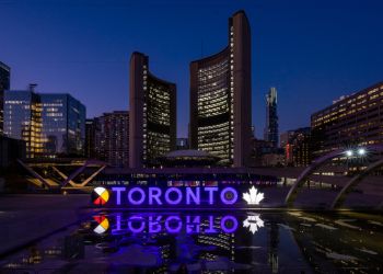 Toronto sign lit purple against a night sky and City Hall in the background.