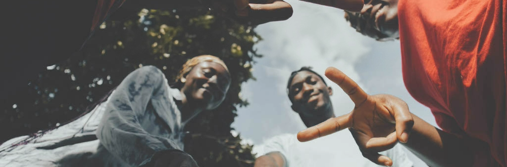 Image of four smiling young Black people holding up peace signs (two fingers).