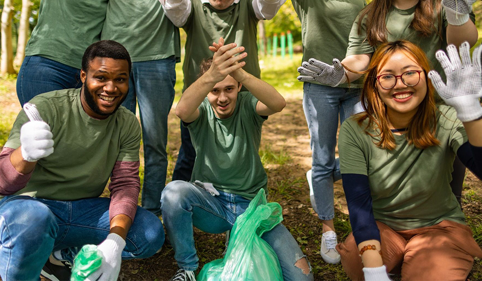 Group of people outside smiling for camera wearing gardening gloves and with green garbage bags