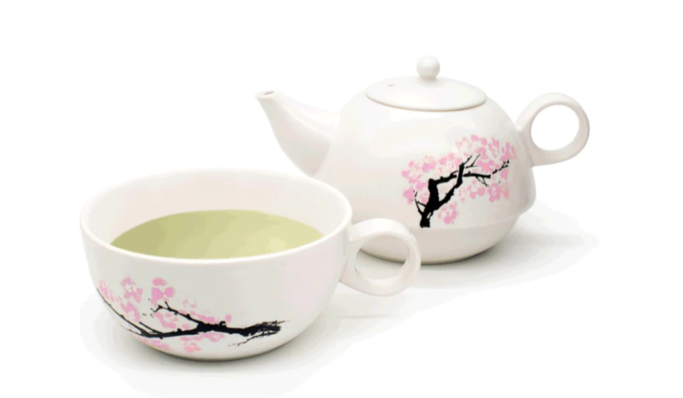Tea cup filled with green tea in front of teapot, both decorated with blooming sakura branches