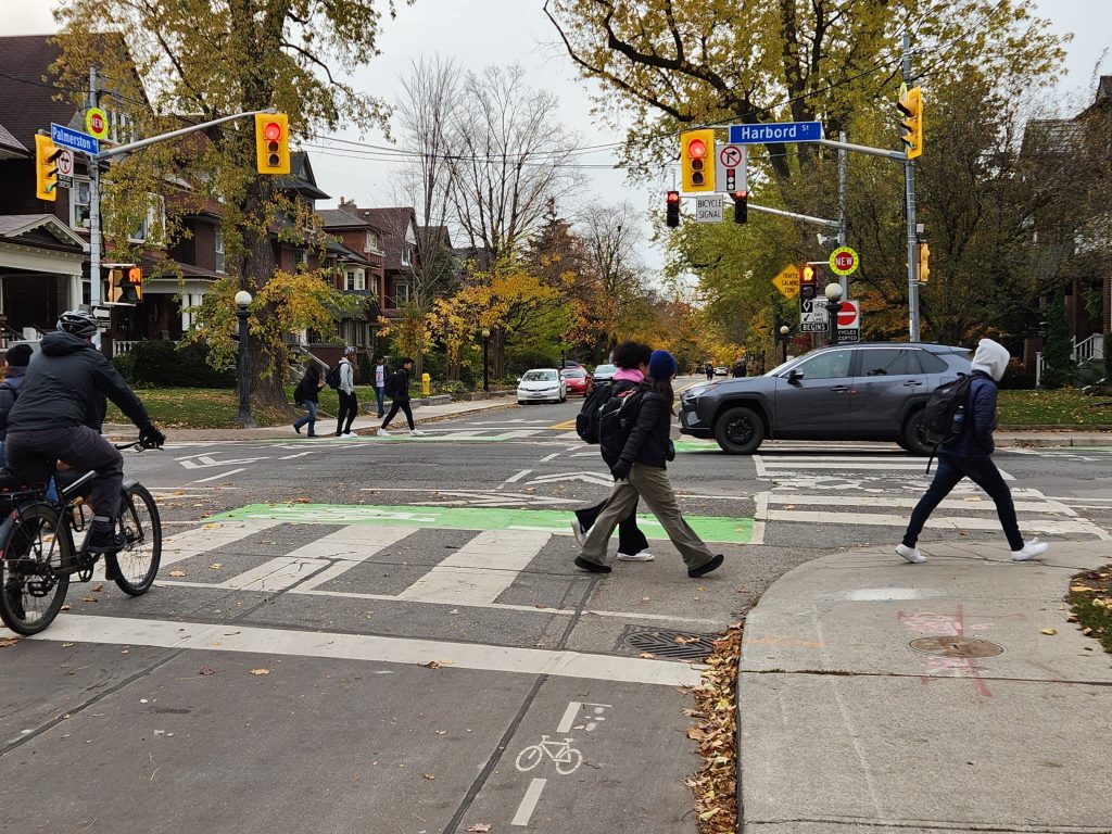 People cycle and walk at an intersection that features bike boxes, bike signals and zebra markings. 