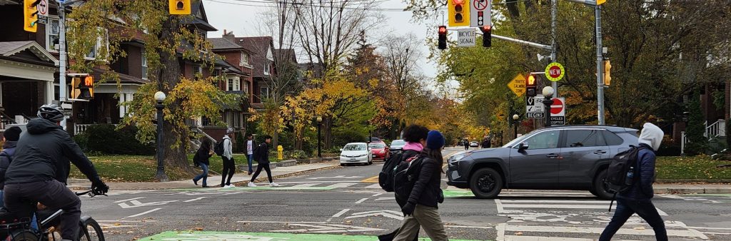 People cycle and walk at an intersection that features bike boxes, bike signals and zebra markings.